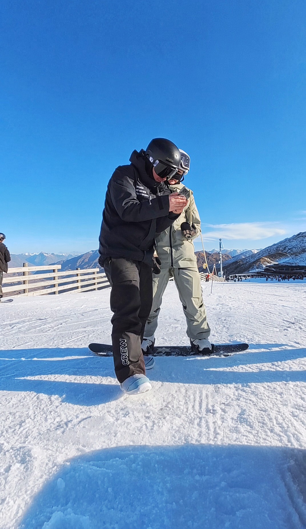 Instructor με μαύρο CREW jacket δείχνει πλάνα σε κινητό σε μαθητή στο χιόνι
